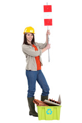 Tradeswoman holding up a traffic sign behind a recycling bin