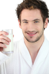 Young man wearing a bathrobe and drinking a glass of milk