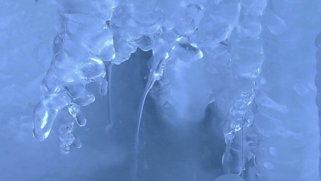 Wassertropfen an Eiszapfen in zugefrorenem Bach