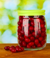 fresh cornel berries in glass jar on green background close-up