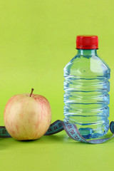 Bottle of water, apple and measuring tape on green background