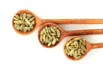 green cardamom in wooden spoons on white background close-up