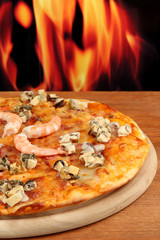 Delicious pizza with seafood on stand on flame background