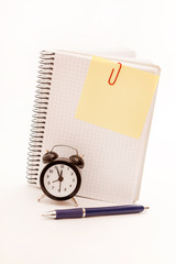 Alarm clock, blank notebook sheet on the white