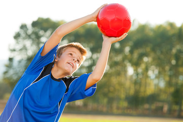 Young boy catching red ball outdoors.