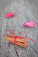 Canela sticks on the background rose petals on wooden texture.