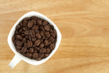 Coffee beans in a cup on wooden background