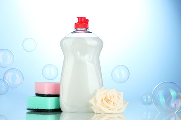 Dishwashing liquid with sponges and flower on blue background