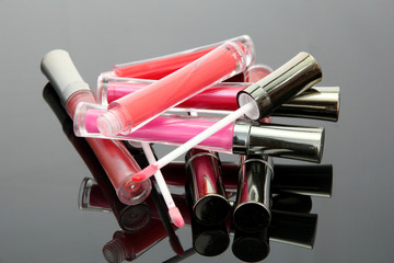 beautiful lip glosses with rose petals, on grey background