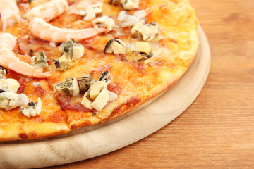 Delicious pizza with seafood on stand on wooden background