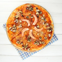 Delicious pizza with seafood on stand on wooden background