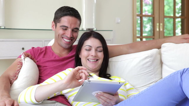 Couple Sitting On Sofa Using Digital Tablet