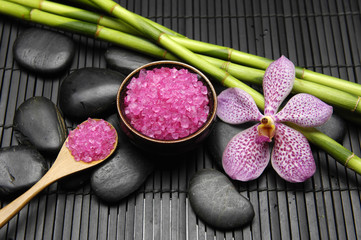 Pink orchid, candle with zen stone and sea salt in spoon on mat