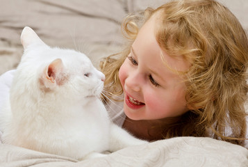 Cute little girl lying in bed with white cat