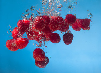 Cluster of raspberries falling into water against white backgrou