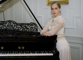 Beautiful young woman dressed in period is based on a piano