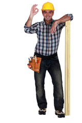 Tradesman leaning on planks of wood and giving the a-ok sign