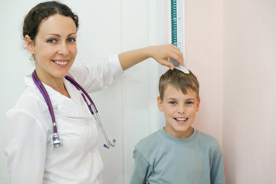 Doctor measures growth boy in medical office, focus on boy