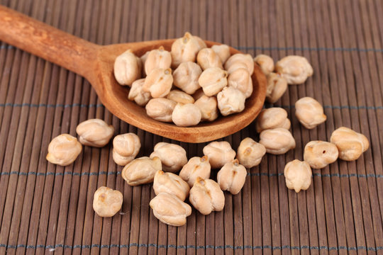 White chickpeas over  wooden spoon on color background
