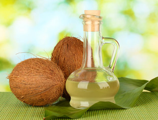 decanter with coconut oil and coconuts on green background