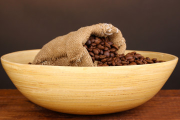 Coffee beans in bowl with bag on table on brown background