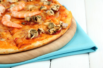 Delicious pizza with seafood on stand on wooden background