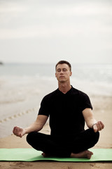 Fototapeta premium Fit young man doing yoga on the beach