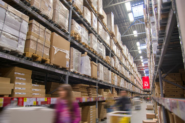 Rows of shelves with boxes in modern warehouse with customers wa