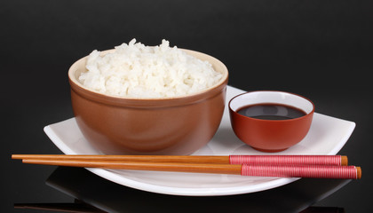 Bowl of rice and chopsticks on plate on grey background