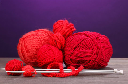 Red knittings yarns on wooden table on purple background