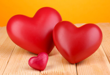 Decorative red hearts on wooden table on orange background