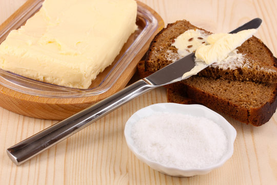 Butter on wooden holder and bread on wooden table close-up