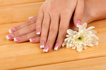 Obraz na płótnie Canvas Woman hands with french manicure and flower on wooden