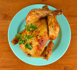 Roasted whole chicken on a blue plate on wooden background