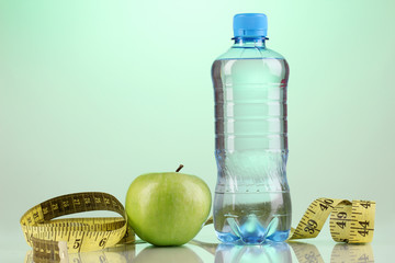 Bottle of water, apple and measuring tape on blue background