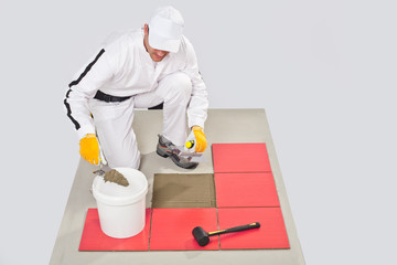 Worker Applies with noched trowel Red Tile on a Floor