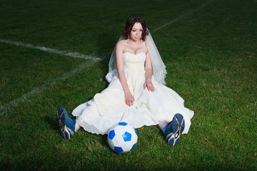 Bride in white dress on a soccer field.