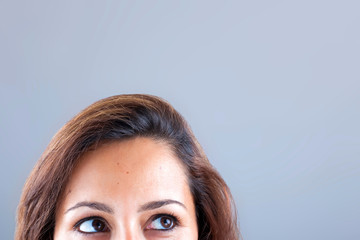 Closeup portrait of a young woman looking up on grey background