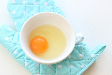 Fresh raw egg in soup cup with blue oven mitt