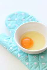 Fresh raw egg in soup cup with blue oven mitt