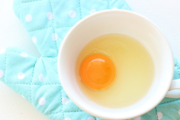 Fresh raw egg in soup cup with blue oven mitt