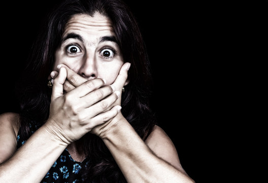 Frightened woman covering her mouth isolated on black