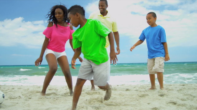 Ethnic parent kicking with soccer ball children on beach