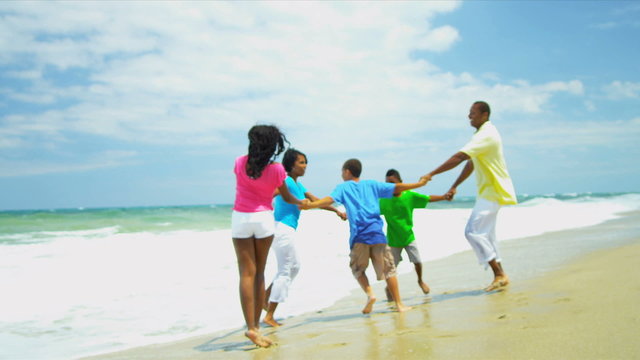 Ethnic family walking on holiday together on beach holding hands 