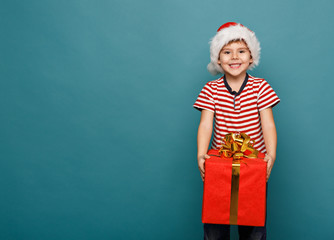 Funny child in Santa red hat holding Christmas gift in hand.