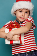 Funny child in Santa red hat holding Christmas gift in hand.