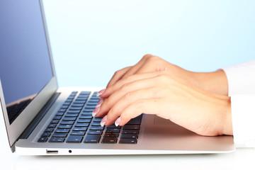 Hands typing on laptop keyboard close up on  blue background
