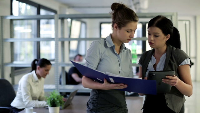 Two young businesswomen with tablet computer and documents in th