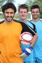 Three smiling footballers with ball