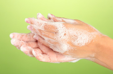 Fototapeta premium Woman's hands in soapsuds, on green background close-up